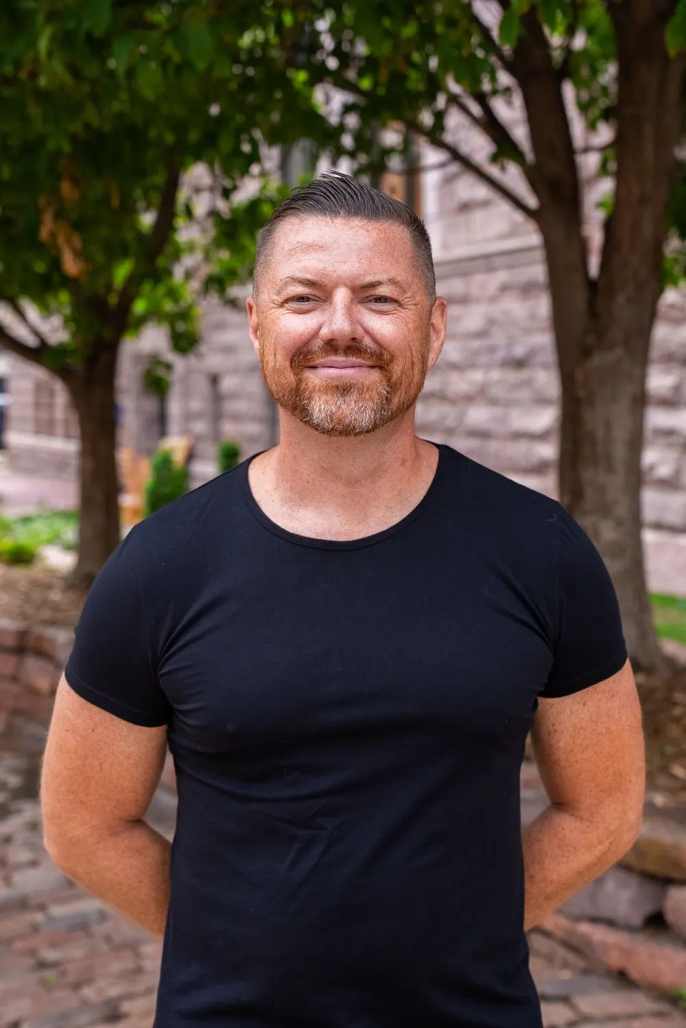 Brian Rand headshot, black t shirt, outdoors
